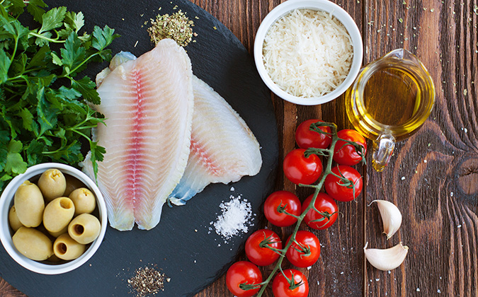Raw tilapia fillets, cherry tomatoes, olives, grated parmesan cheese and provencal herbs - ingredients for mediterranean style baked fish with vegetables